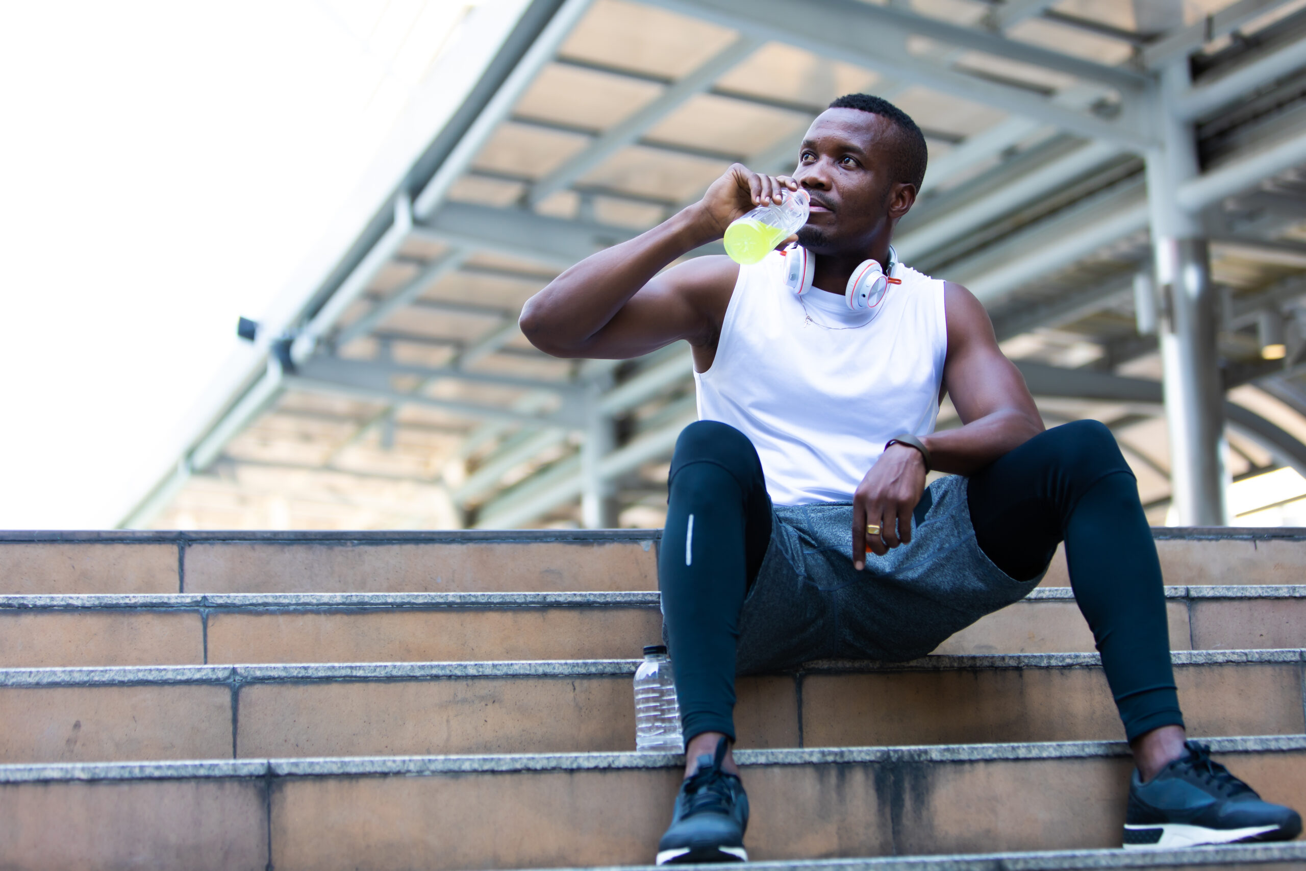 Happy good healthy and wellness concept. fitness, sport, workout people and lifestyle concept. African american man sweating taking a break listening to music on phone after workout sitting on Stair at the city morning
