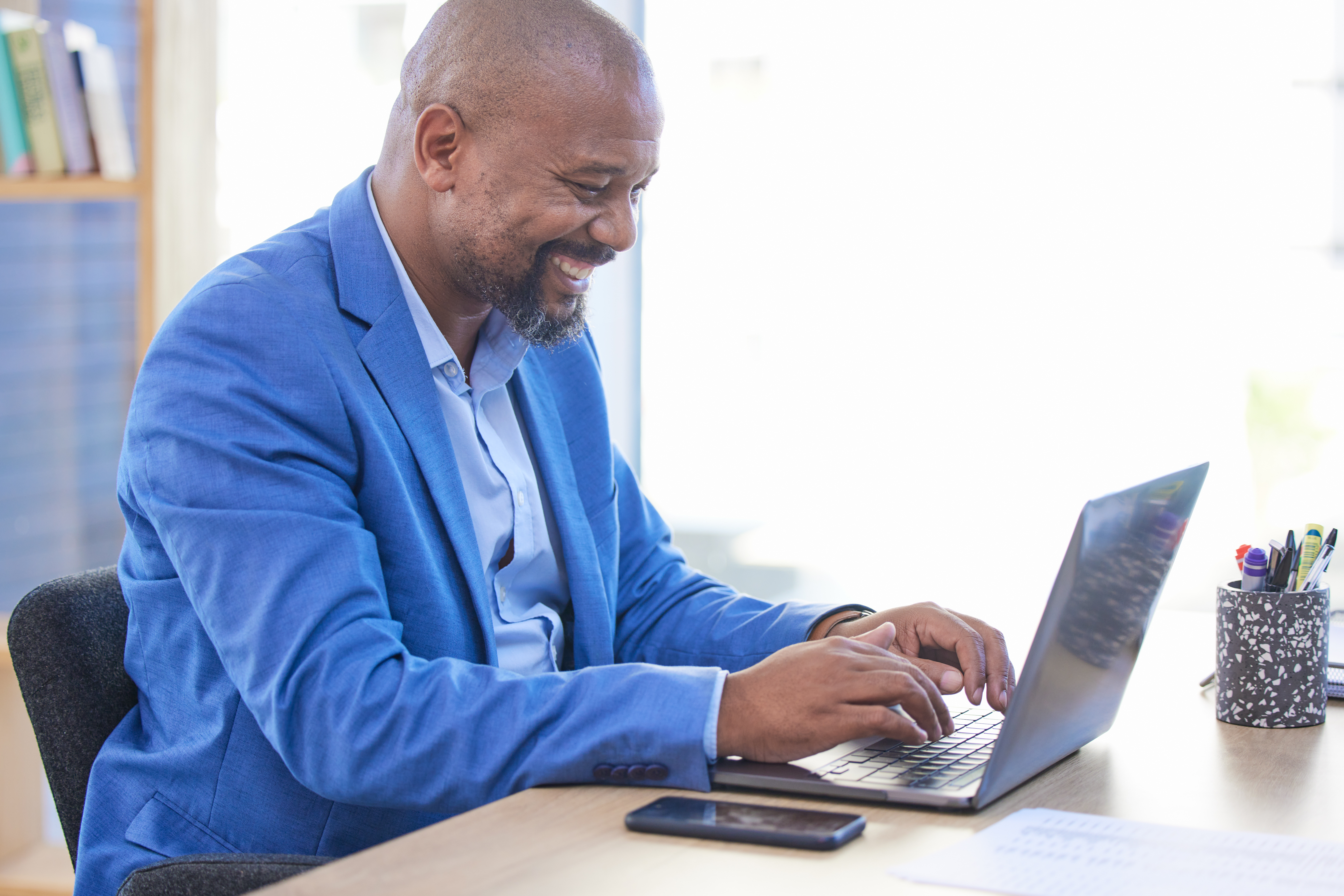 Business man, laptop and smile while typing communication, email or social media post at work. Black man, happy and computer for online research, office and writing to client, employee or customer.