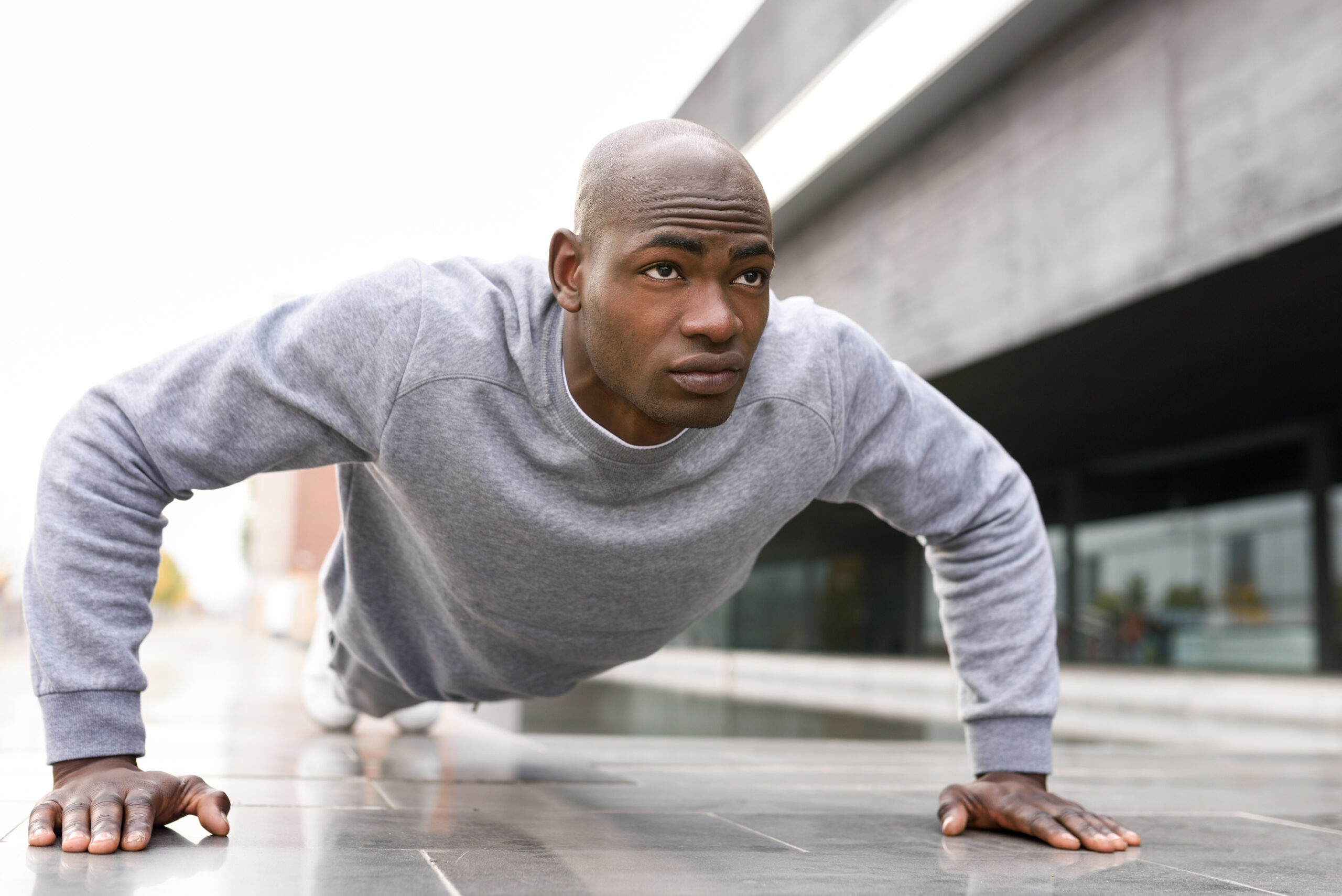 Fitness black man exercising push ups. Male model cross-training in urban background  African guy in his twenties doing workout outdoors in the street.